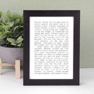 May include: A black rectangular frame containing a white print with black typewriter-style text about Pilates. The text begins with 'Whoever thinks ten seconds goes by really quickly has never been to a pilates class.' The word Pilates is in red.