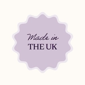 May include: A light purple, scalloped-edge sticker with the words "Made in THE UK" in a dark purple script and sans-serif font. The sticker is set against a cream-colored background.