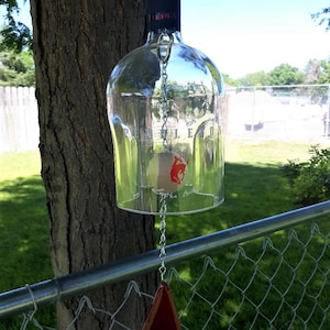 May include: A glass wind chime made from a clear wine bottle with a red label that says "Pennington" and a red triangle-shaped chime at the bottom.