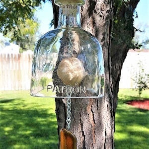 May include: A glass wind chime made from a Patron tequila bottle with a cork stopper and a brown glass piece hanging from a silver chain.