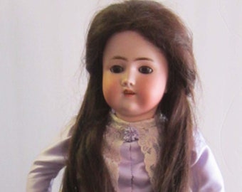 Puede incluir: Muñeca antigua de porcelana con cabello largo y castaño, vestida con un vestido lavanda con ribetes de encaje.