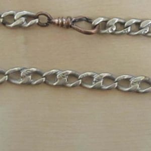 May include: A silver chain necklace with a copper clasp. The chain is made of interlocking links.