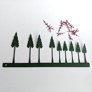 May include: A row of ten dark green paper trees with a dark green paper base. There are several small, red paper sprigs scattered above the trees.
