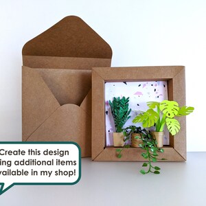 May include: A brown paper frame with a white background and three paper plants inside. The plants are green and have a 3D effect. The frame is sitting on a white surface. "Create this design using additional items available in my shop!" is written in a speech bubble.