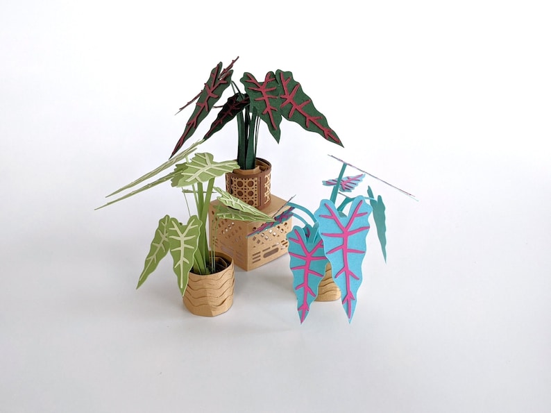 May include: Three papercraft potted plants with different colored leaves. The plants are in brown pots with a woven pattern. The leaves are green, red, and blue.