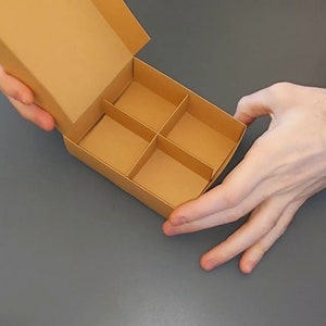 May include: A brown cardboard box with four compartments, open and held by two hands.