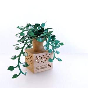 May include: A green paper plant with a brown paper pot sits on top of a brown paper box with a lattice design. The plant is hanging over the sides of the box.