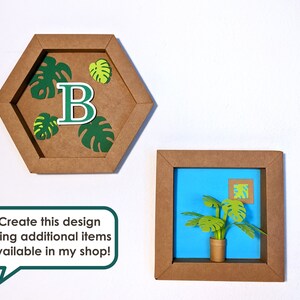 May include: Two brown paper frames with a blue background. The first frame is a hexagon with a green monstera leaf design and the letter "B" in the center. The second frame is a square with a green monstera plant in a brown pot.