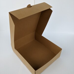 May include: A brown cardboard box with a flap top and a small handle. The box is open and empty.