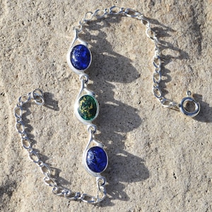 May include: A silver chain bracelet with three round glass charms. The charms are blue, green with gold flecks, and blue.