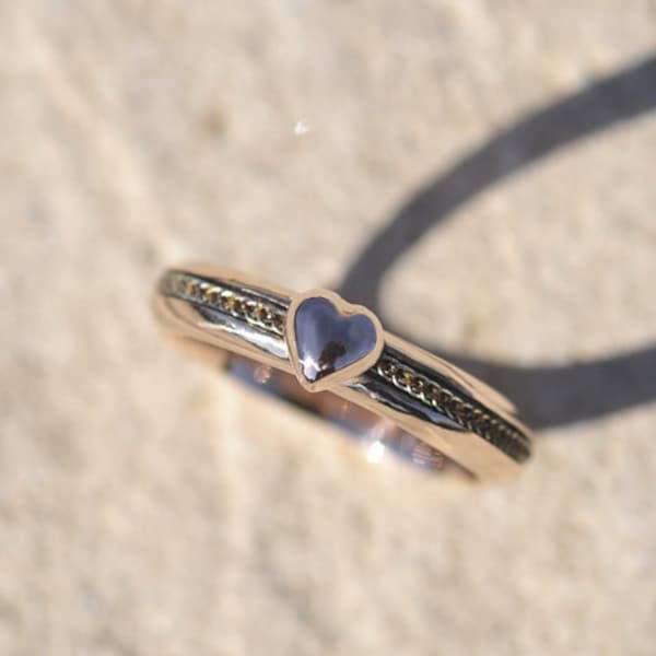 Könnte beinhalten: Ein goldener Ring mit einem herzförmigen Design. Das Herz ist dunkler als der Ring und hat eine strukturierte Oberfläche.