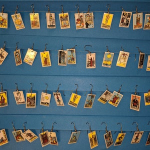 Può includere: Una parete con 40 orecchini a forma di carte dei tarocchi. Le carte sono disposte in file e sono tutte diverse. Le carte sono tutte in una cornice bianca con un bordo dorato. Gli orecchini sono tutti in argento.