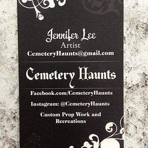 May include: Black and white business card with a skull and floral design. The card reads "Jennifer Lee, Artist, Cemetery Haunts@gmail.com, Cemetery Haunts, Facebook.com/Cemetery Haunts, Instagram: @Cemetery Haunts, Custom Prop Work and Recreations."