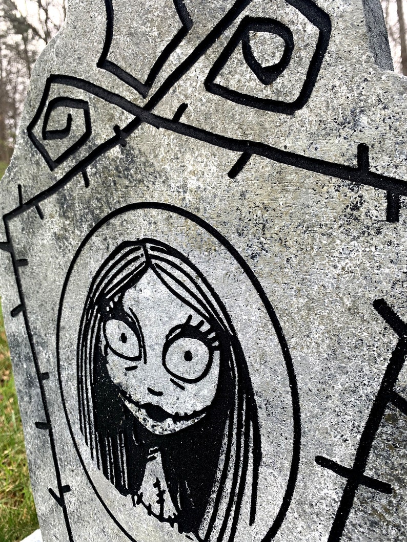 May include: A black and white illustration of a character from the film The Nightmare Before Christmas. The character is a woman with long black hair, large eyes, and a stitched mouth. The illustration is on a grey, textured background.