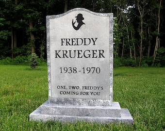 May include: A grey tombstone bearing the name "FREDDY KRUEGER" and the dates "1938-1970". The tombstone features a silhouette of a fedora-wearing figure and the inscription "ONE, TWO, FREDDY'S COMING FOR YOU" at the base.