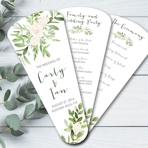 May include: Wedding ceremony program fan with a floral design. The fan features a white background with green leaves and white flowers. The text on the fan reads "The Wedding of Carly & Ian, August 27, 2016, Agoura Hills, CA".