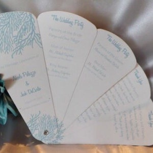 May include: White wedding program fan with a blue and white sea coral design. The fan has the text "The Wedding Party" and the names of the wedding party members. The fan also has the text "Thank You" on the back.