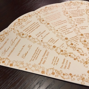 May include: A white wedding fan with gold ornate designs and text. The text reads "Welcome to... Bavarian Wedding... Join Us As We... Celebrate... Grow Old Along with Me, The Best Is Yet To Be... Robert Browning... Bavaria Germany... May 23, 2015... Zwei Herzen Eine Die Liebe Für Immer... Two Hearts One Love Forever".