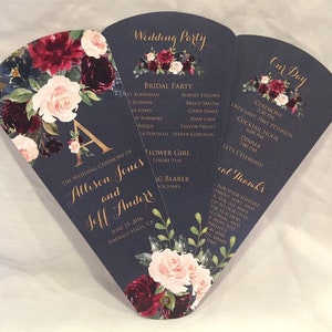 Könnte beinhalten: Ein blauer Hochzeitsprogramm-Fächer mit einem floralen Design in den Farben Burgunderrot, Rosa und Weiß. Der Text auf dem Fächer lautet "Wedding Party" und "Our Day" mit den Details der Hochzeitszeremonie und einer Liste der Hochzeitsgesellschaft.