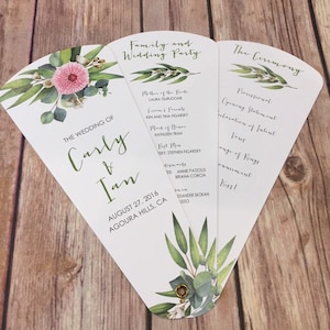 May include: A white wedding program fan with green and pink floral illustrations. The program includes the wedding ceremony order, the wedding party, and the wedding date and location. The text reads "The Wedding of Carly & Ian, August 27, 2016, Agoura Hills, CA."