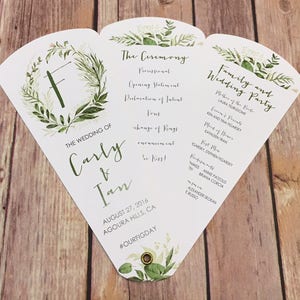 May include: A white wedding programme fan with green foliage and the text "The Wedding of Carly & Ian" and "The Ceremony" and "Family and Wedding Party".