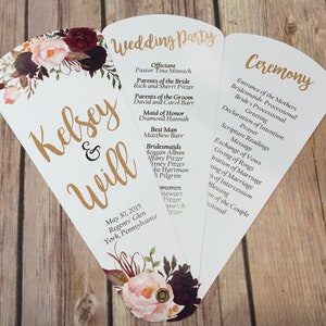 Könnte beinhalten: Ein Hochzeits-Programm-Fächer mit einem floralen Design in den Farben Rosa, Burgunderrot und Grün. Das Programm listet die Hochzeitsgesellschaft, die Zeremoniedetails und das Datum und den Ort der Hochzeit auf: 30. Mai 2015, Regents Glen, York, Pennsylvania.