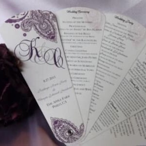 Könnte beinhalten: Ein Hochzeitszeremonie-Programm-Fächer mit einem Paisley-Muster in Violett- und Weißtönen. Der Fächer enthält das Hochzeitsdatum, die Namen des Paares und die Reihenfolge der Zeremonie. Der Text ist in einer formellen Schriftart.