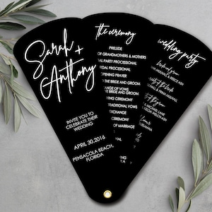 Könnte beinhalten: Schwarzer Hochzeitsfächer mit weißem Kalligraphietext. Der Fächer listet die Namen "Sarah + Anthony" und Details der Zeremonie auf, einschließlich der Hochzeitsgesellschaft und des Datums. Ein einzigartiges Hochzeitsaccessoire.