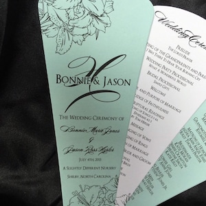 Könnte beinhalten: Ein hellblauer und weißer Fächer für eine Hochzeitszeremonie mit floralen Designs. Das Programm enthält die Reihenfolge der Ereignisse, die Namen des Brautpaares, Bonnie Marie Jones und Jason Russ Herter, sowie das Datum der Hochzeit, den 4. Juli 2015. Das Programm enthält auch die Namen der Hochzeitsgesellschaft.