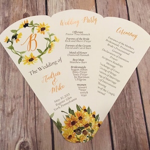 Könnte beinhalten: Ein Hochzeitsfächer mit einem Sonnenblumenmuster. Das Programm enthält die Namen der Hochzeitsgesellschaft, des Standesbeamten und die Details der Zeremonie. Die Hochzeit ist für Andrea und Mike und findet am 30. Mai 2015 in Regents Glen in York, Pennsylvania, statt.