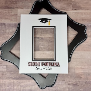 May include: A white mat with a black border and a black frame. The mat has a rectangular opening and features a graduation cap graphic and the text "SOUTH CAROLINA Class of 2026" in maroon and black.