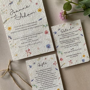 May include: A wedding invitation suite with a floral design. The invitation is printed on seed paper and features the names "Joanne and Adam" in cursive script. The details card includes the date, time, and location of the wedding ceremony and reception. The gifts card explains that the couple has already received many gifts and would prefer monetary donations for their honeymoon.