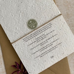 May include: A white card made from recycled paper with embedded wildflower seeds. The card has a brown twine tied around it and a green circle logo that says "love grows". The card includes instructions on how to plant the seeds: "1. In Spring/Summer... 2. Place in a pot of compost... 3. Keep the soil and paper moist... 4. Once your small plants have grown, place pot outside or keep on a window that has lots of sun." The card is signed "Vida Design."