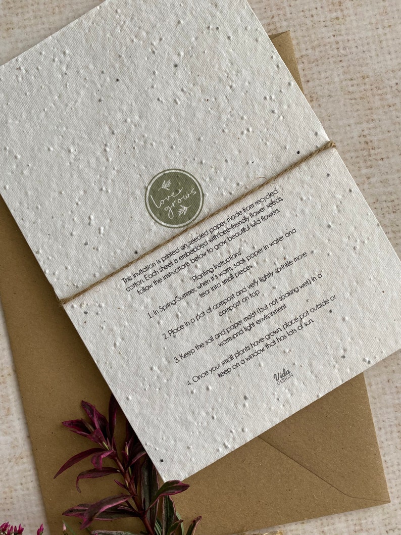 May include: A white card made from recycled paper with embedded wildflower seeds. The card has a brown twine tied around it and a green circle logo that says "love grows". The card includes instructions on how to plant the seeds: "1. In Spring/Summer... 2. Place in a pot of compost... 3. Keep the soil and paper moist... 4. Once your small plants have grown, place pot outside or keep on a window that has lots of sun." The card is signed "Vida Design."