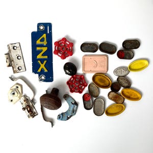 May include: A collection of vintage hardware components, including a blue metal plate with "4NZX" in yellow, red valve handles, and various metal pieces in shades of silver, brown, and yellow. The items are arranged on a white surface.
