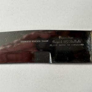K&ouml;nnte beinhalten: Nahaufnahme einer Edelstahl-Messerklinge mit gezahnter Kante. Die Klinge tr&auml;gt die Aufschrift "STAINLESS FOREVER SHARP" und "Peeredge Regent (PJ) Sheffield BLADE MADE IN ENGLAND". Der Griff ist verchromt.