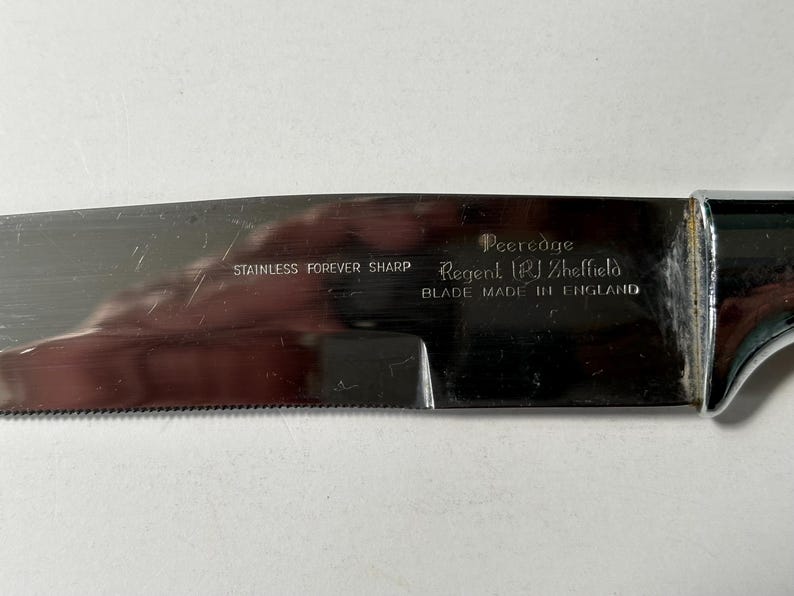 K&ouml;nnte beinhalten: Nahaufnahme einer Edelstahl-Messerklinge mit gezahnter Kante. Die Klinge tr&auml;gt die Aufschrift "STAINLESS FOREVER SHARP" und "Peeredge Regent (PJ) Sheffield BLADE MADE IN ENGLAND". Der Griff ist verchromt.