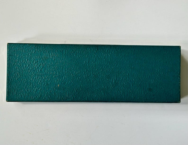 K&ouml;nnte beinhalten: Eine rechteckige, teal-farbene Box mit strukturierter Oberfl&auml;che. Die Box ist geschlossen und scheint aus einem strapazierf&auml;higen Material zu bestehen. Die Box befindet sich vor einem wei&szlig;en Hintergrund.