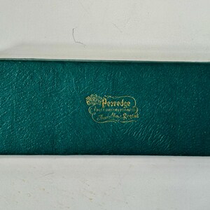 K&ouml;nnte beinhalten: Eine rechteckige, teal-farbene Box mit strukturierter Oberfl&auml;che. Auf der Box steht in goldener Schrift "Pezredge, Finest Sheffield Cutlery, Trafalgar House, Regent."