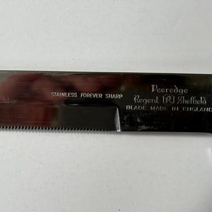 K&ouml;nnte beinhalten: Ein gezahntes Messer aus Edelstahl mit gl&auml;nzender Klinge und Chromgriff. Die Klinge ist mit den Texten "STAINLESS FOREVER SHARP" und "Peeredge Regent Sheffield BLADE MADE IN ENGLAND" beschriftet.