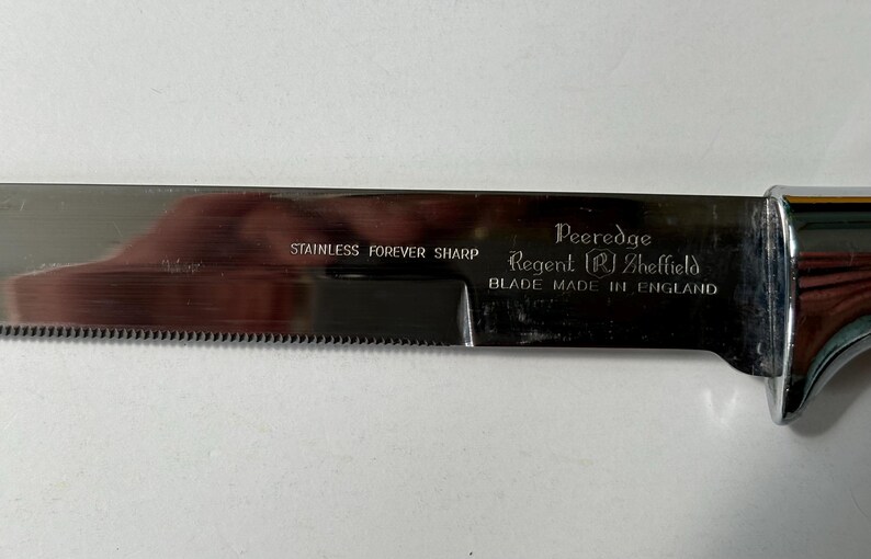 K&ouml;nnte beinhalten: Ein gezahntes Messer aus Edelstahl mit gl&auml;nzender Klinge und Chromgriff. Die Klinge ist mit den Texten "STAINLESS FOREVER SHARP" und "Peeredge Regent Sheffield BLADE MADE IN ENGLAND" beschriftet.