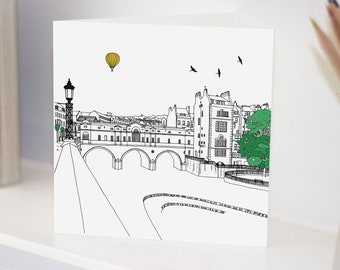 May include: A black and white line drawing of a bridge with buildings on either side. A yellow hot air balloon is floating in the sky above the bridge. There are birds flying in the sky.
