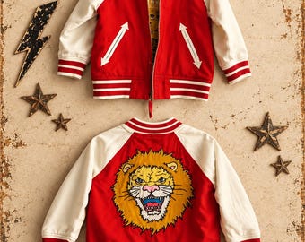Puede incluir: Una chaqueta tipo varsity roja y crema con cremallera frontal, detalles de bolsillos en forma de flecha blanca y ribetes a rayas. La espalda muestra un gráfico grande y detallado de una cabeza de león rugiendo.