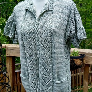 May include: A light green knitted top with a collar and short sleeves. The top has a lace pattern and two pockets.