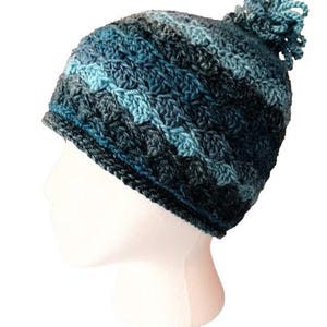 May include: A blue and black crocheted beanie with a fluffy pom pom on top.