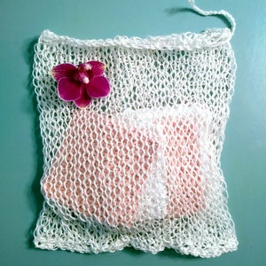 May include: White mesh laundry bag with a pink knitted insert and a pink orchid flower on top.