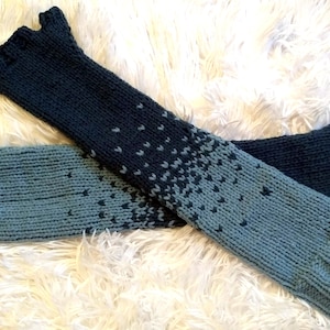 May include: A pair of long, knitted arm warmers in a gradient of blue and black. The arm warmers have a textured pattern and are made of soft yarn.