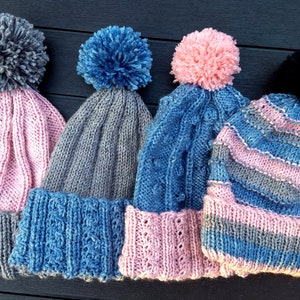 Peut inclure: Quatre bonnets en tricot avec des pompons de différentes couleurs, dont le rose, le gris, le bleu et le noir. Les bonnets ont des motifs et des textures de tricot différents.