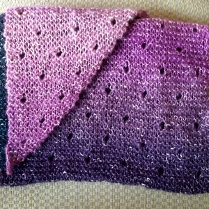 May include: A purple and pink knitted scarf with a lacy pattern. The scarf is made with a gradient yarn that transitions from a darker purple to a lighter pink.