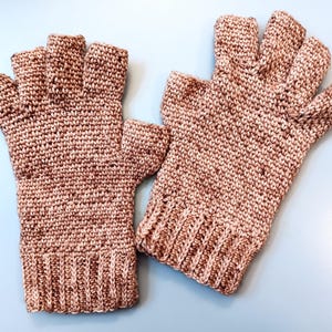 Op de afbeelding: Een paar vingerloze handschoenen in een gespikkelde bruine en tan kleur. De handschoenen zijn gebreid met een geribbelde manchet en open vingers. De handschoenen worden gepresenteerd op een lichtblauwe ondergrond.